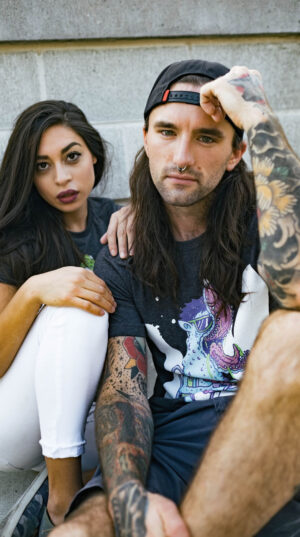 A man and woman sitting on the ground with tattoos.