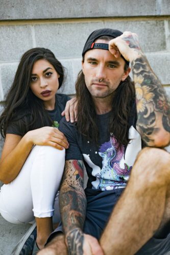 A man and woman sitting on the ground with tattoos.