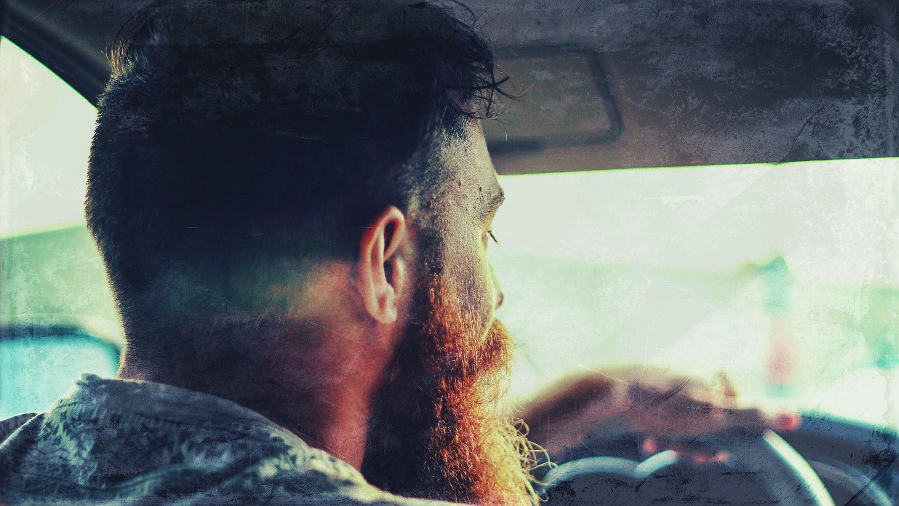 A man with red beard sitting in the backseat of a car.