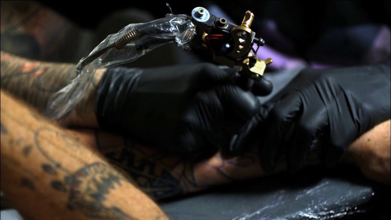 A person with black gloves on holding onto a tattoo machine.