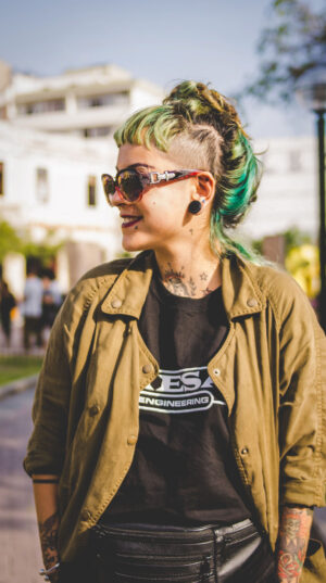 A woman with green hair and sunglasses standing on the street.