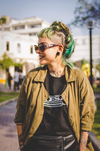 A woman with green hair and sunglasses standing on the street.
