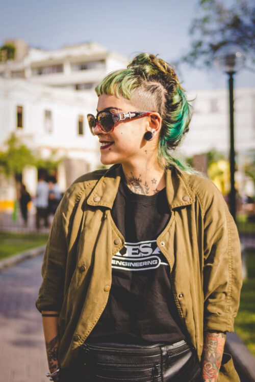 A woman with green hair and sunglasses standing on the street.