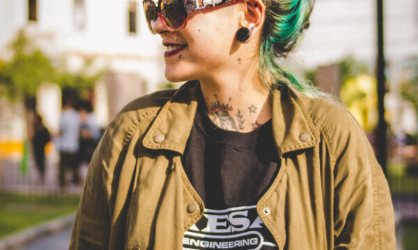 A woman with green hair and sunglasses standing on the street.