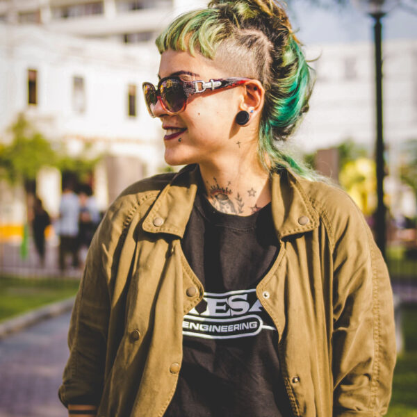 A woman with green hair and sunglasses standing on the street.