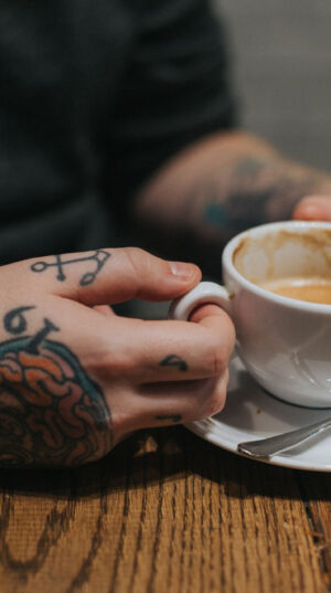 A person with tattoos holding a cup of coffee.