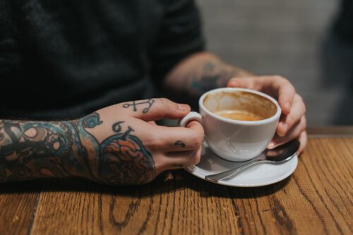 A person with tattoos holding a cup of coffee.