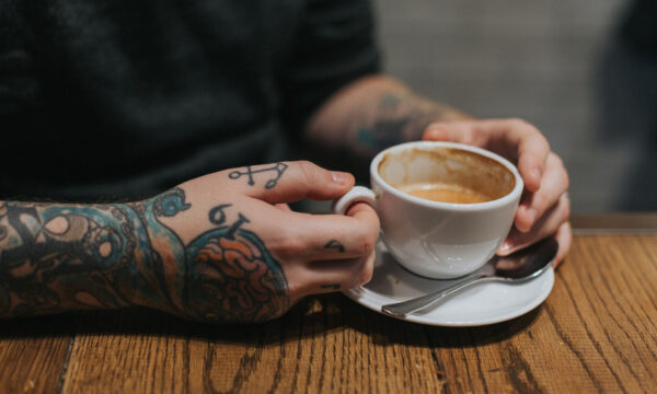 A person with tattoos holding a cup of coffee.