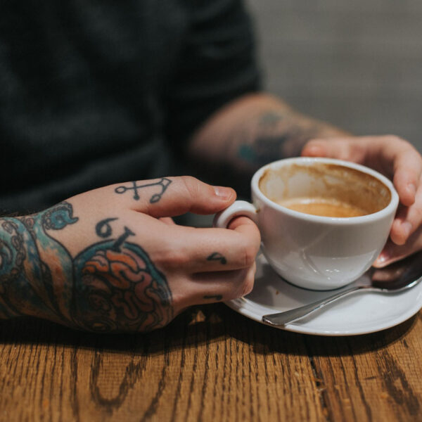 A person with tattoos holding a cup of coffee.